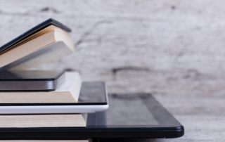 A stack of books and digital tablets symbolizing the transition from physical documents to digital formats, representing paper to digital conversion services.